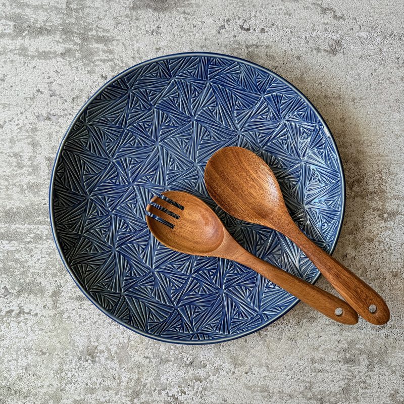 Blue textured dinner plate with wooden salad servers.
