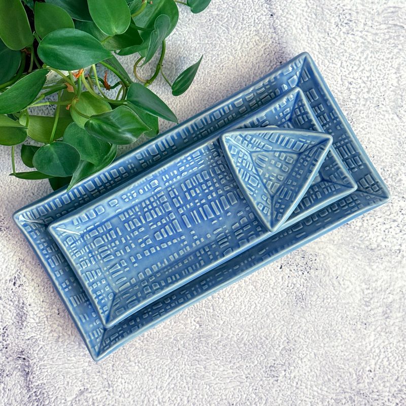 Blue rectangular tray with patterned small dishes and greenery.