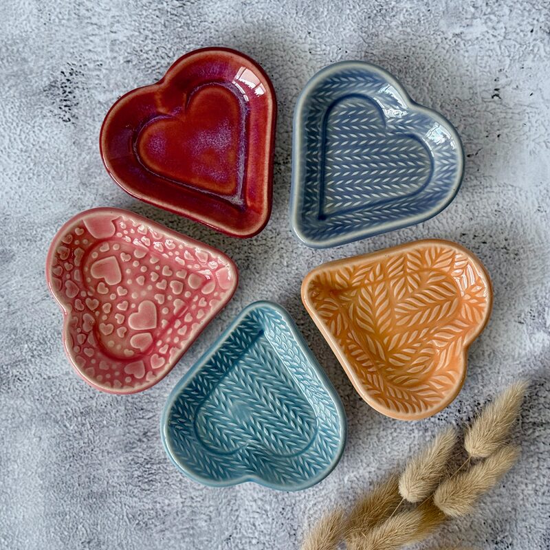 Assortment of five small heart-shaped ceramic dishes in blue, pink, red and orange glazes arranged together
