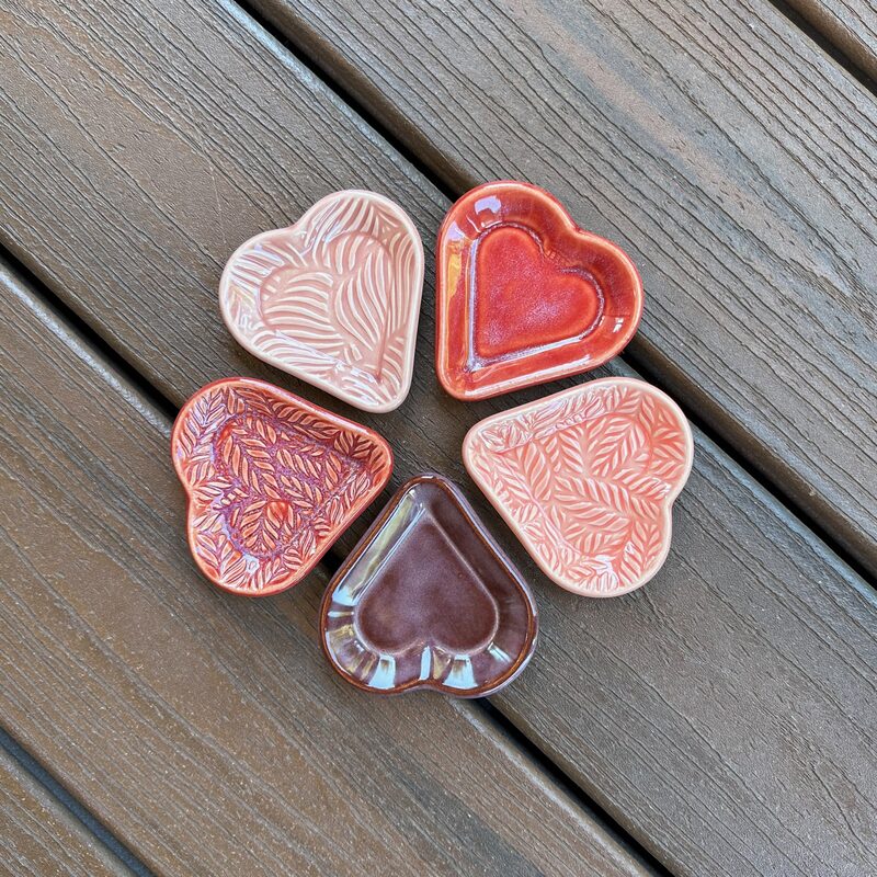 Circle of small pink and burgundy heart-shaped ceramic trinket dishes arranged on wooden boards